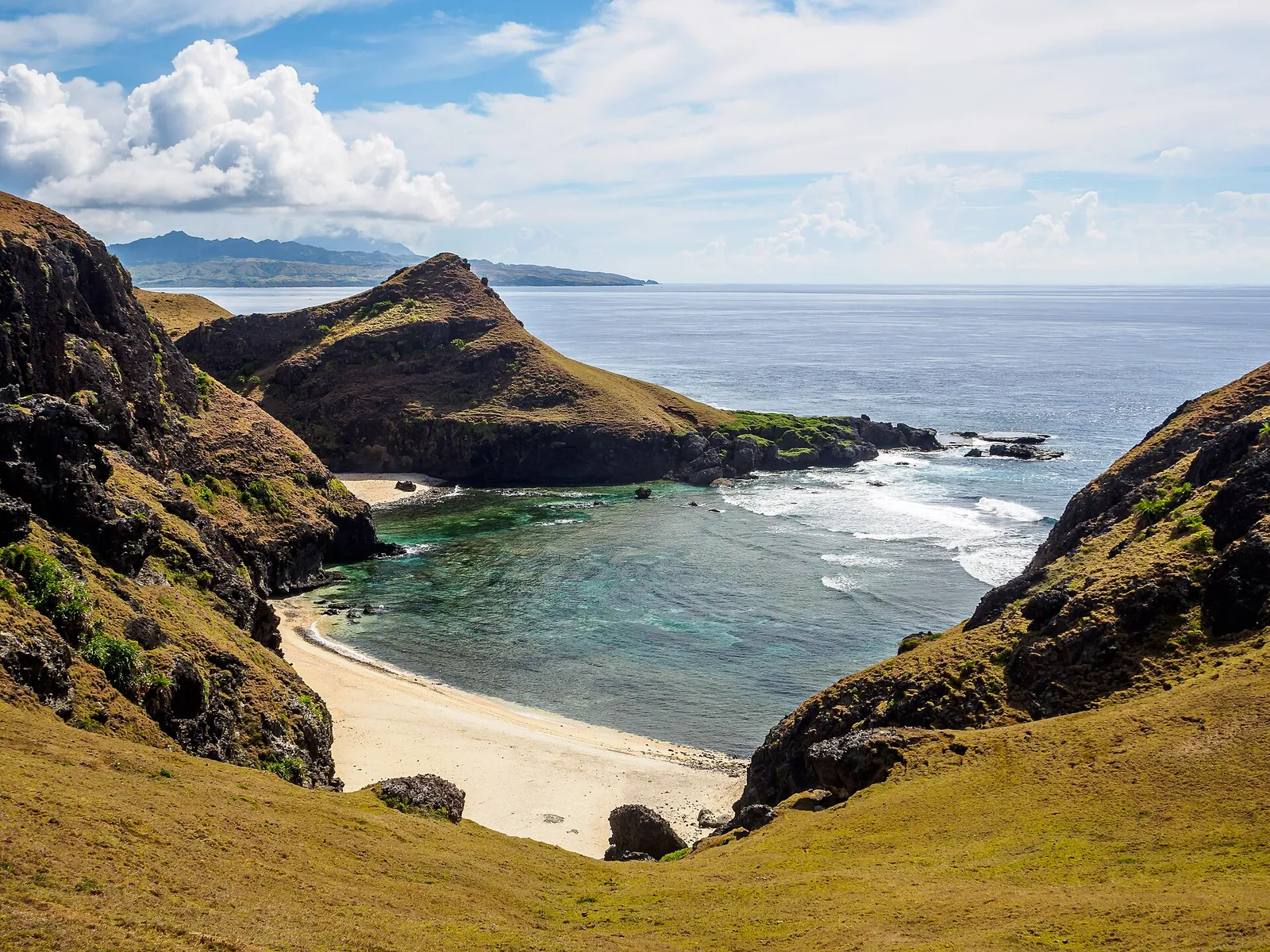 Green and rocky headlands surrounding a sandy cove on Sabtang Island