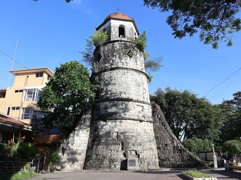 Stone belfry rising beside trees under a clear blue sky in Dumaguete