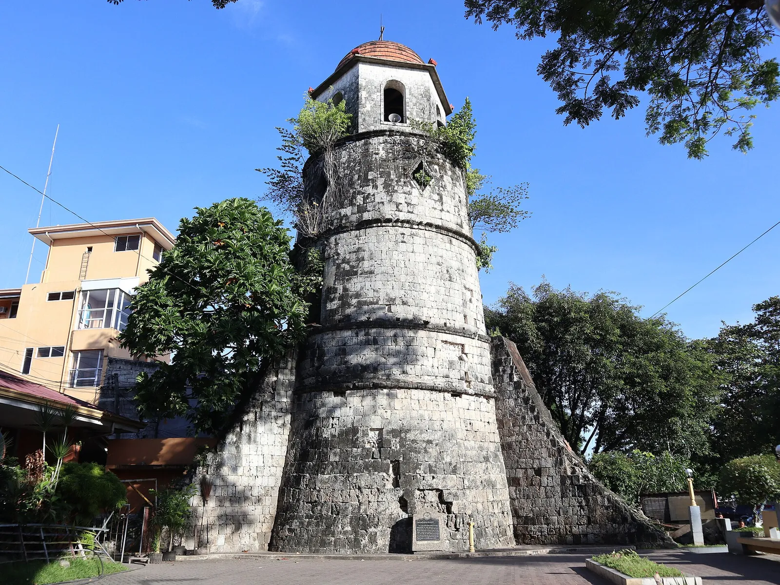 Stone belfry rising beside trees under a clear blue sky in Dumaguete