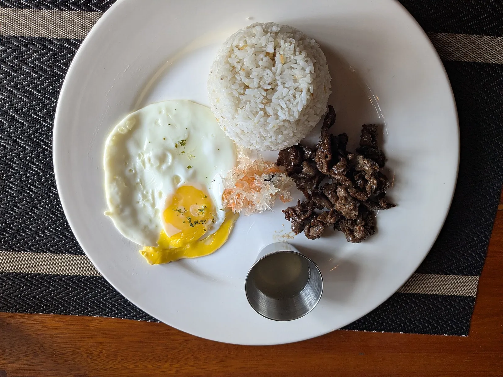 Rice, a fried egg, beef pieces and pickled papaya on a breakfast plate