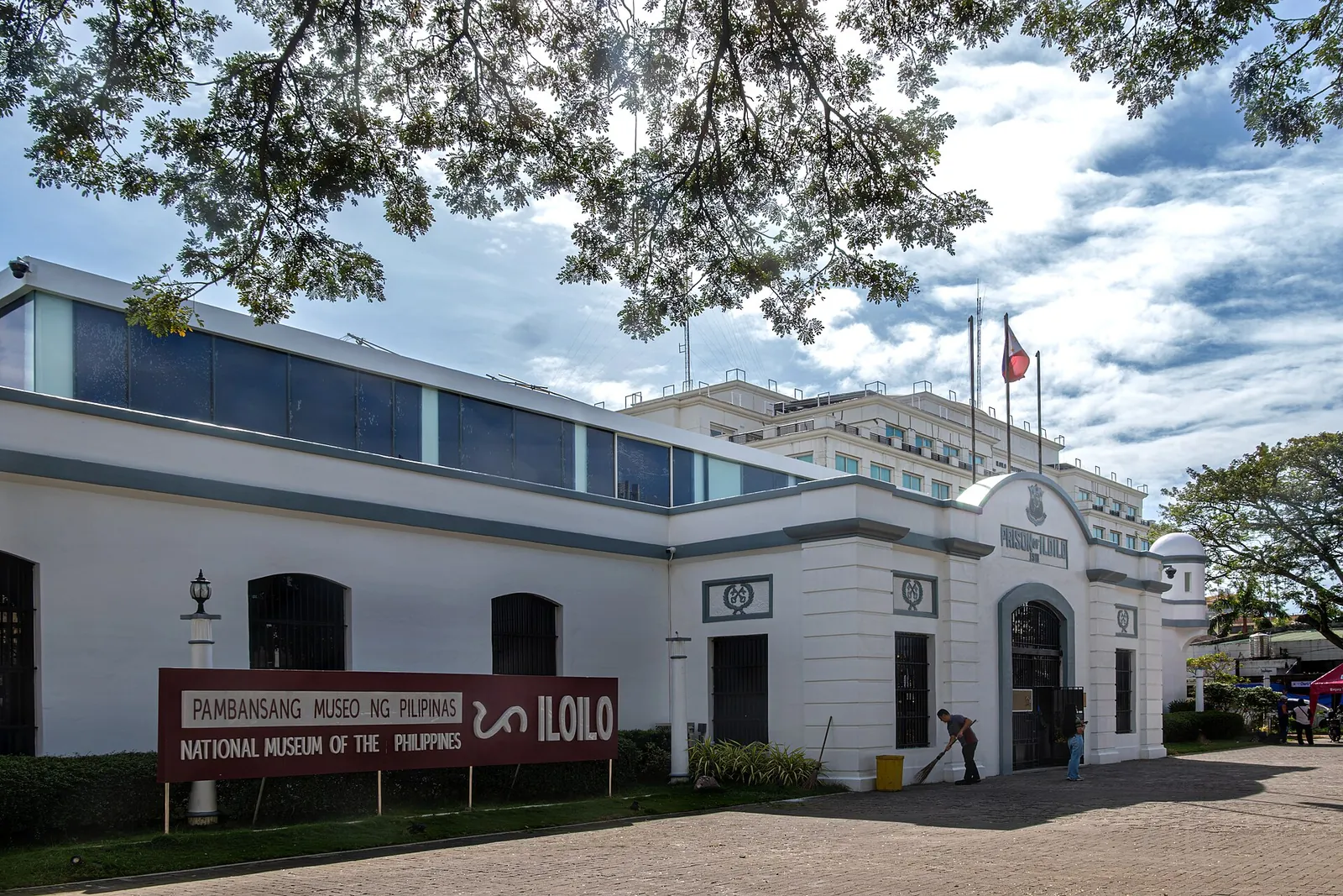 National Museum building in Iloilo City beneath leafy branches and a cloudy sky