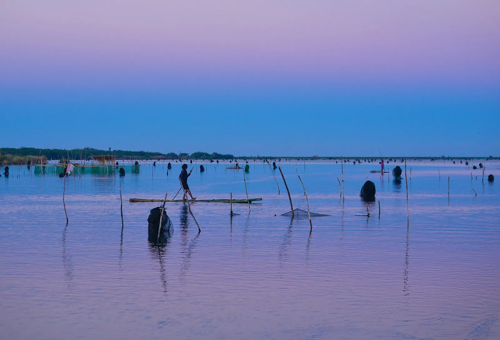 People standing in shallow water along the Padsan River in morning light in Laoag