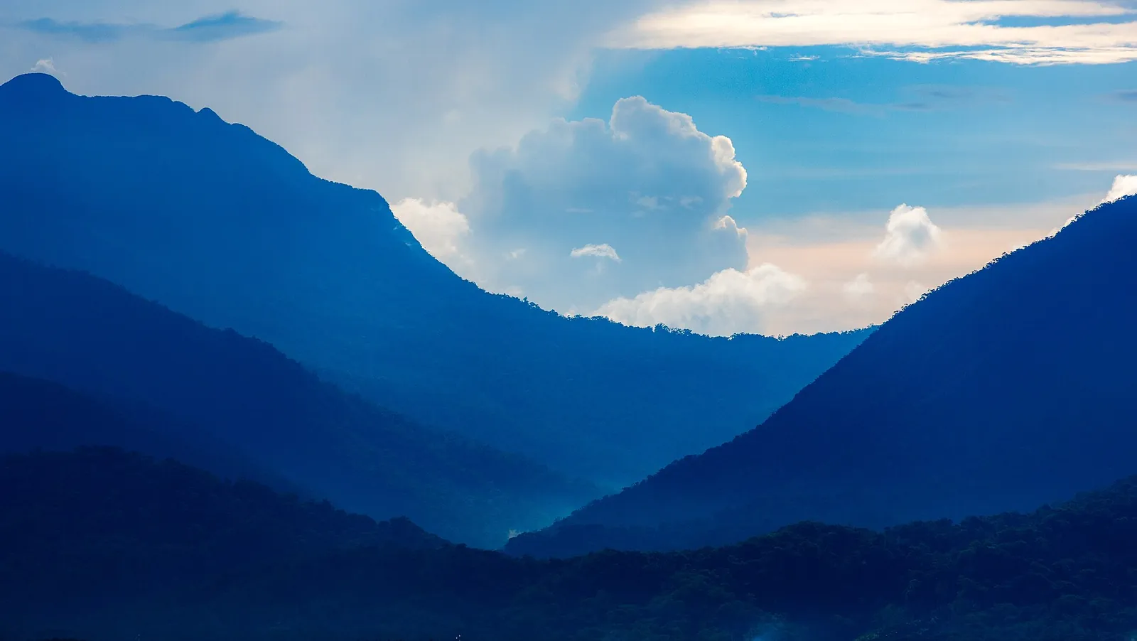 Layered blue mountains beneath clouds seen across the water from Puerto Princesa Baywalk