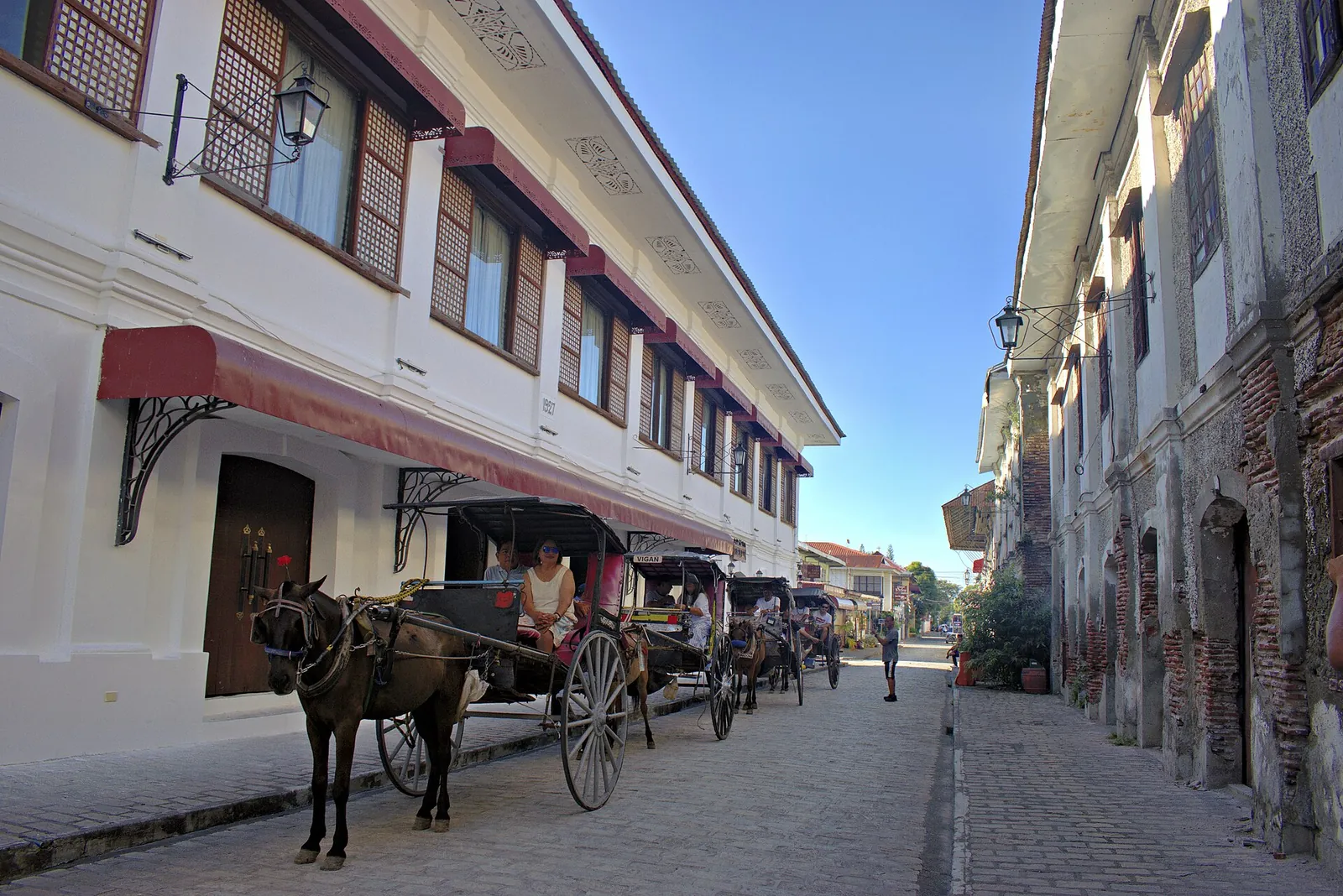 Horse-drawn carriages beside white heritage facades on Calle Crisologo in Vigan