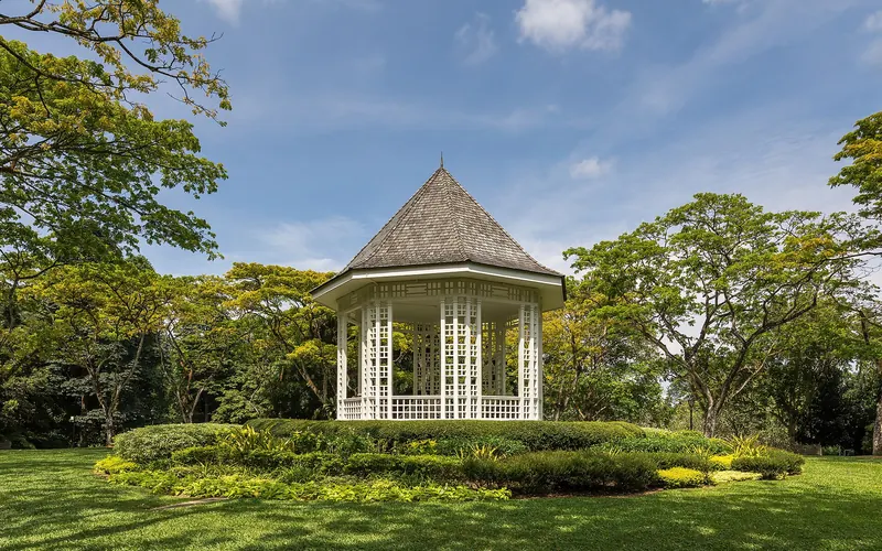 Weißer Musikpavillon zwischen grünen Bäumen und sonnigem Rasen in den Singapore Botanic Gardens