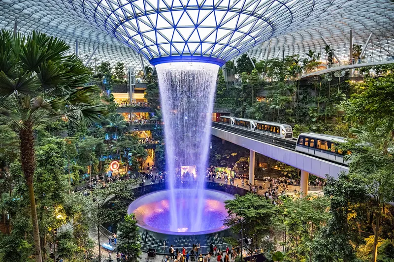 Wodospad Rain Vortex spływa przez szklaną kopułę Jewel na lotnisku Changi, a obok przejeżdża Skytrain