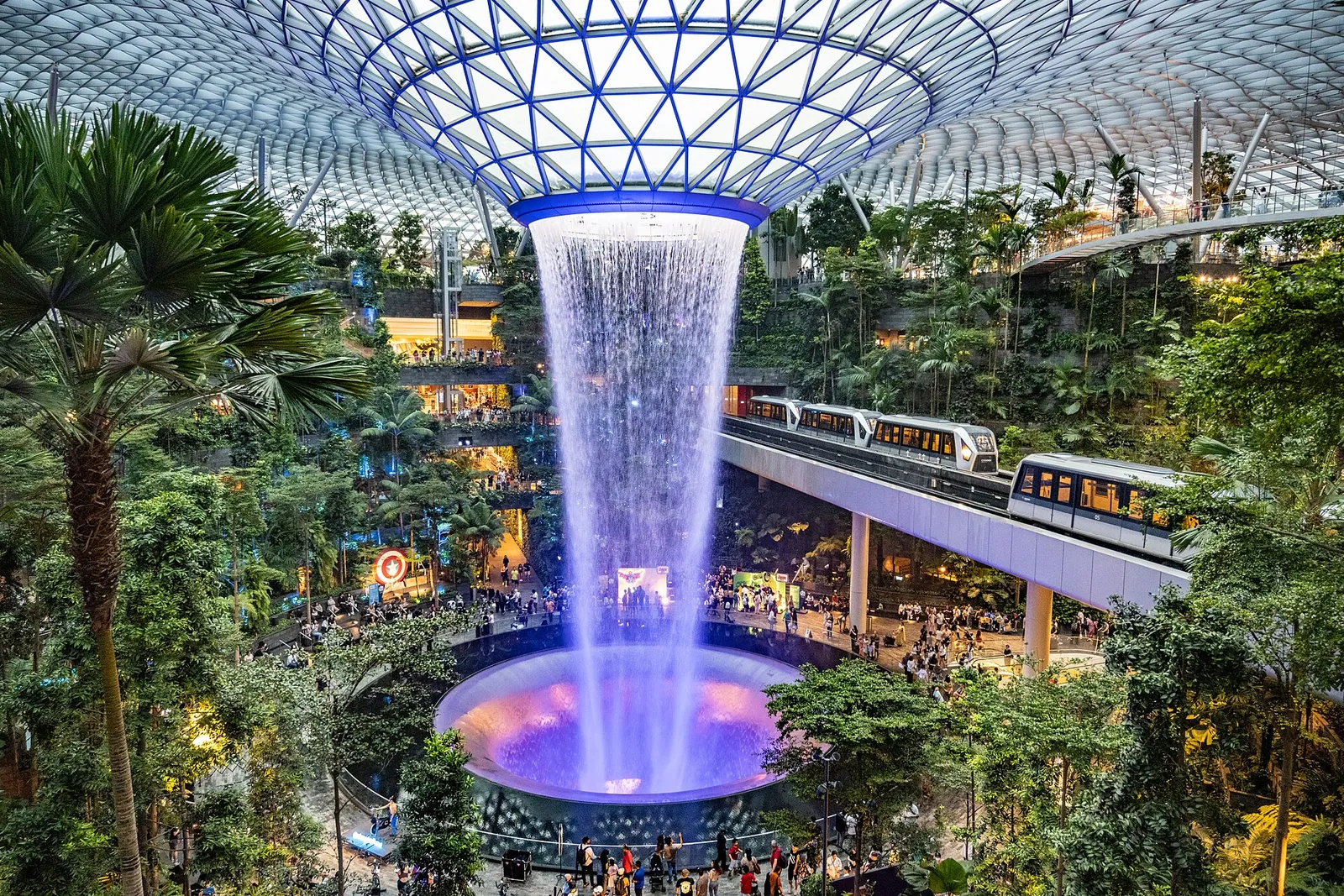 Der Wasserfall Rain Vortex fällt durch die Glaskuppel des Jewel am Flughafen Changi, während der Skytrain vorbeifährt