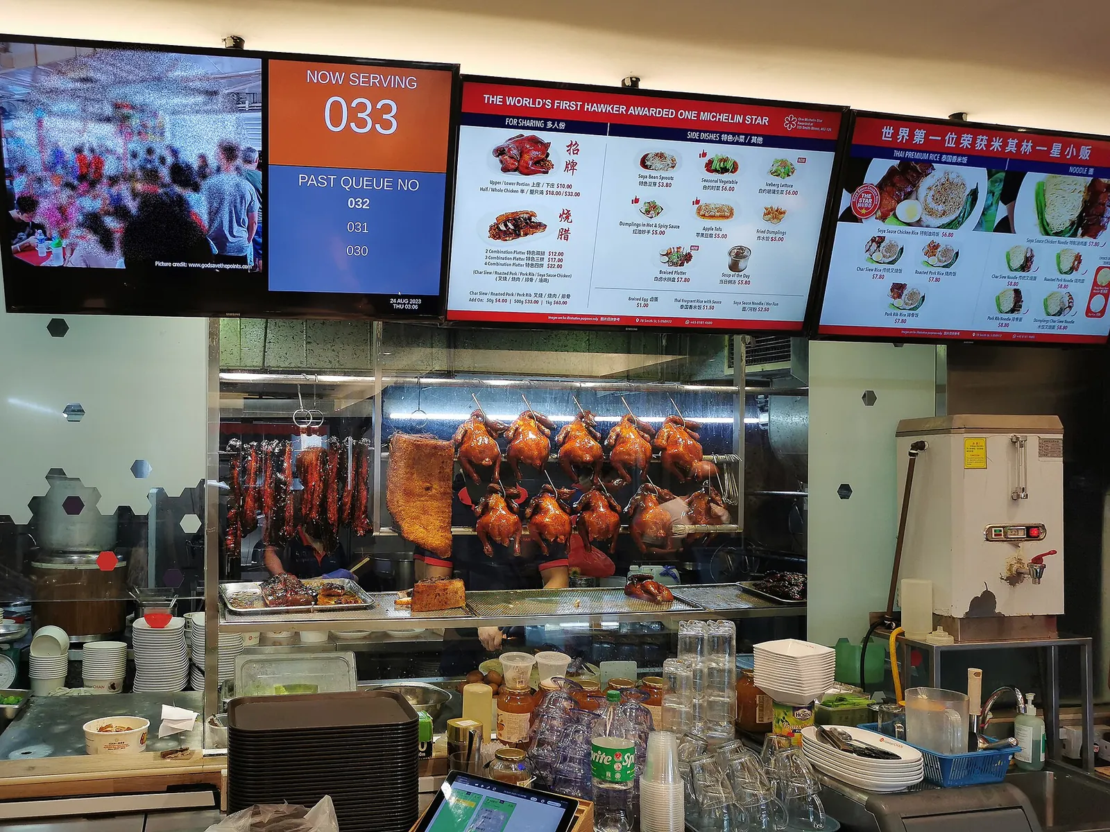 Tabule nabídky a zavěšená pečená masa v Hawker Chan na Smith Street v Singapuru