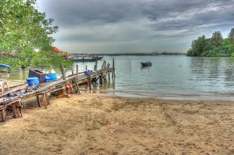 Boote an einem sandigen Ufer und hölzernen Anlegeplatz auf Pulau Ubin