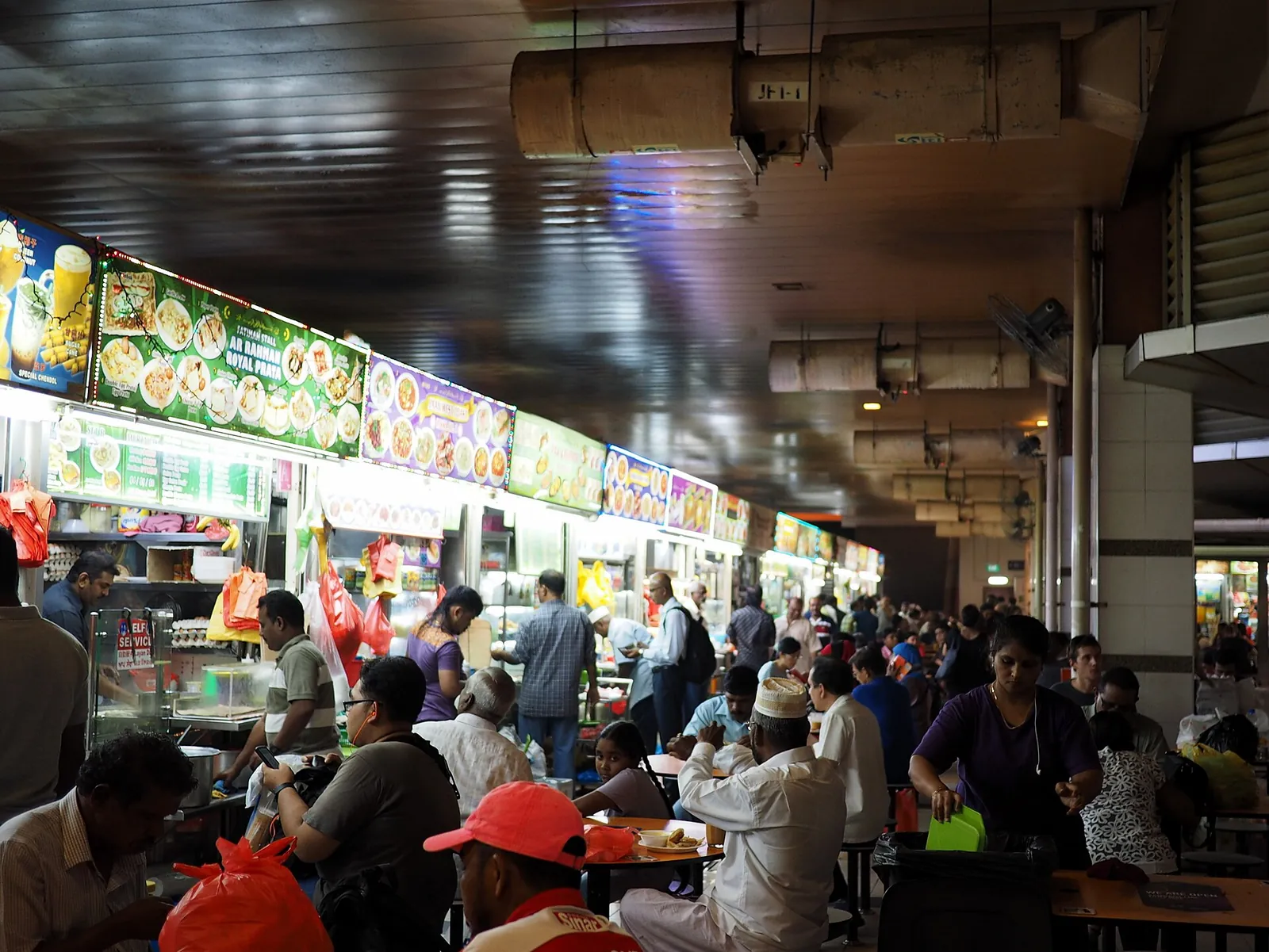 Gäste sitzen neben einer Reihe von Hawker-Ständen im Tekka Centre in Singapur
