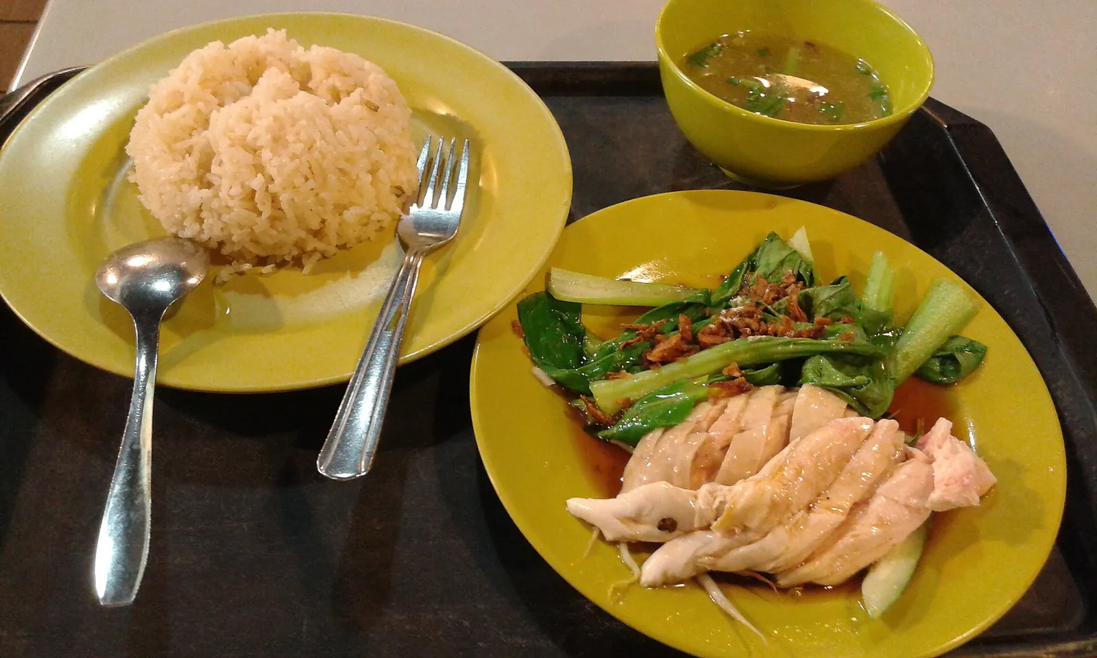 Sliced chicken, rice, vegetables and soup on yellow plates in Singapore