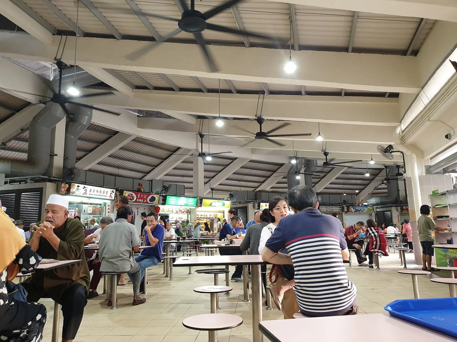 Diners seated at tables beneath ceiling fans in a Singapore hawker centre