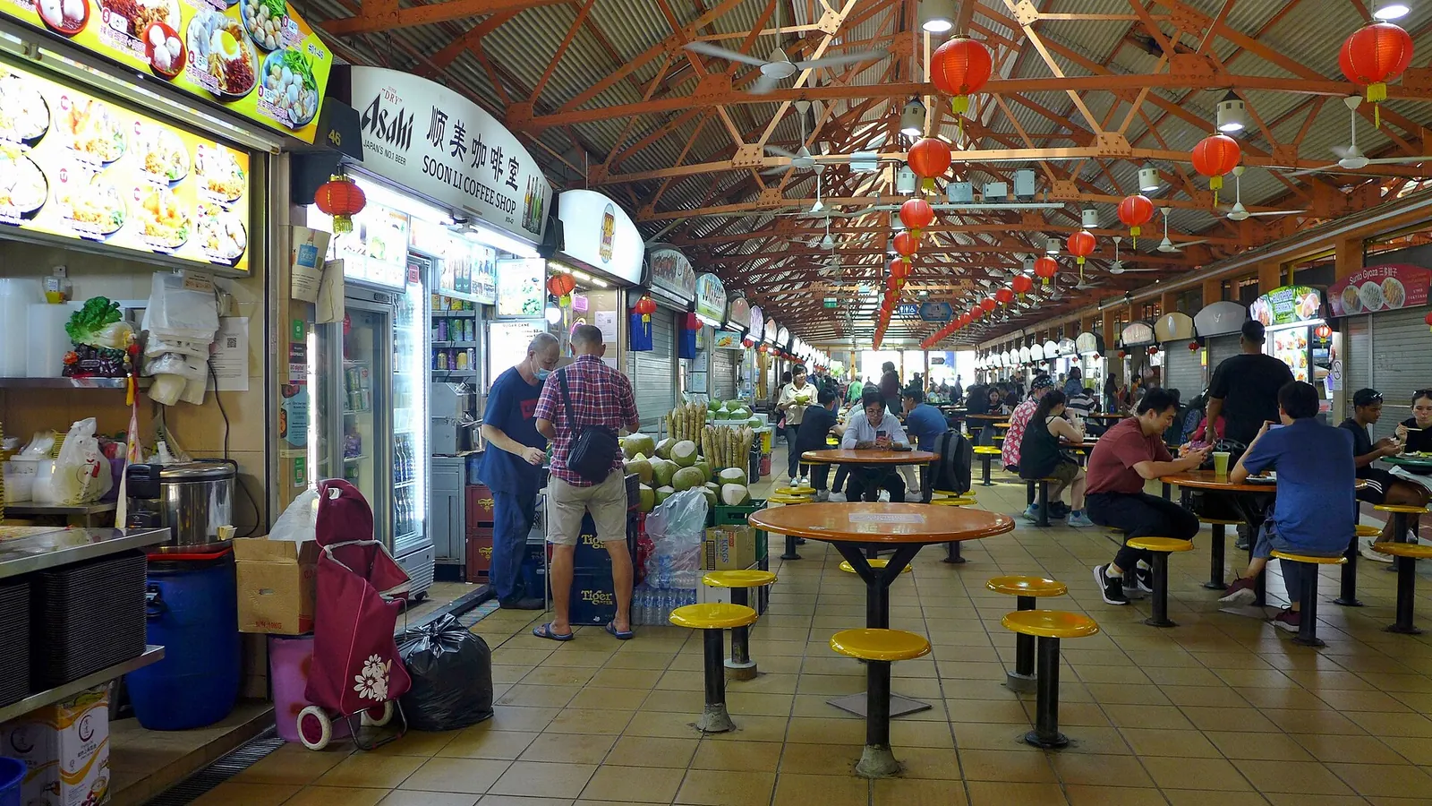 Řady osvětlených stánků a stolů uvnitř Maxwell Food Centre pod červenými lampiony