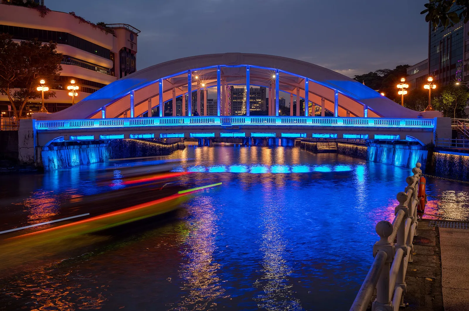 En båt passerer under opplyste Elgin Bridge på Singapore River