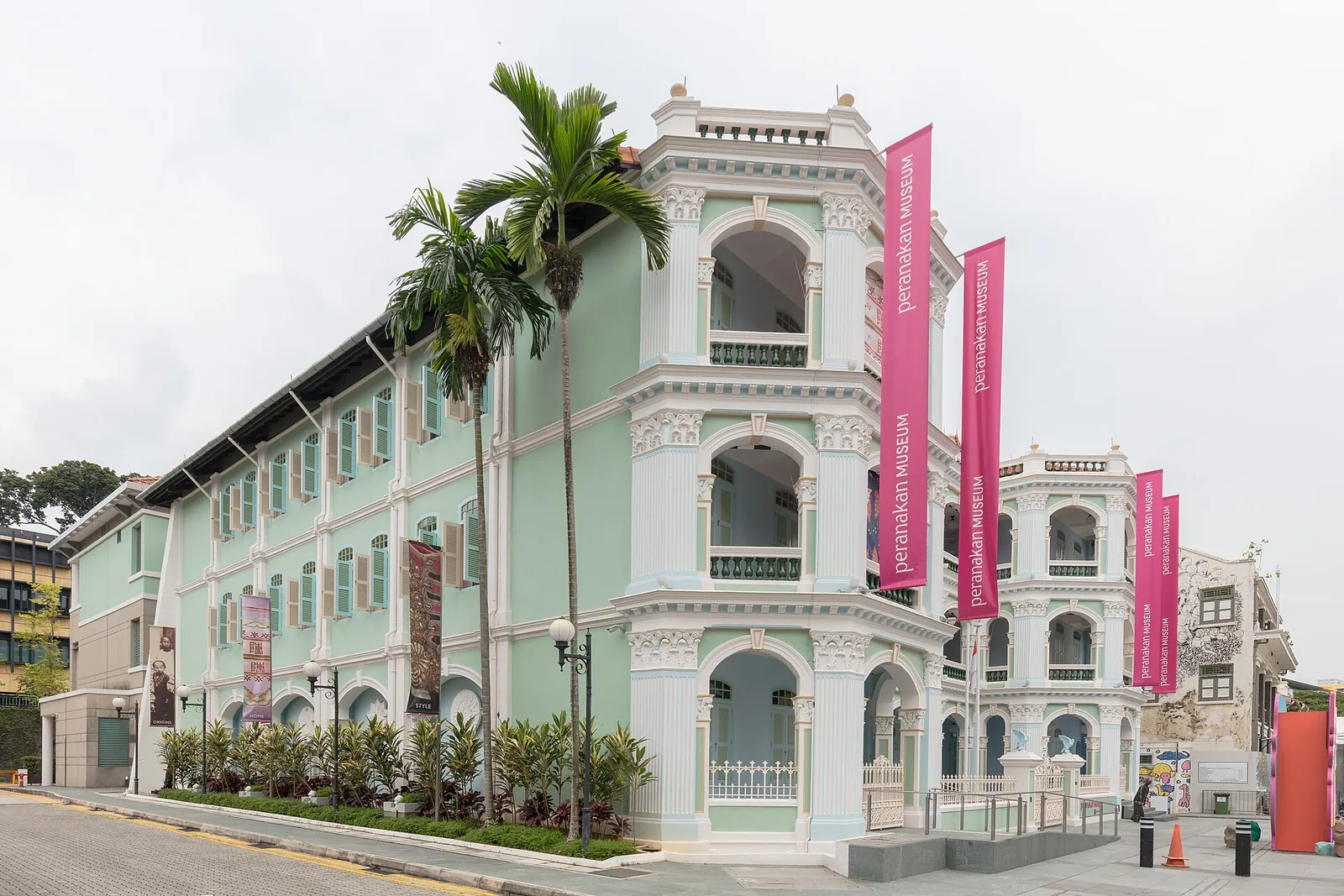 Světle zelená fasáda Peranakan Museum s bílými oblouky a palmami