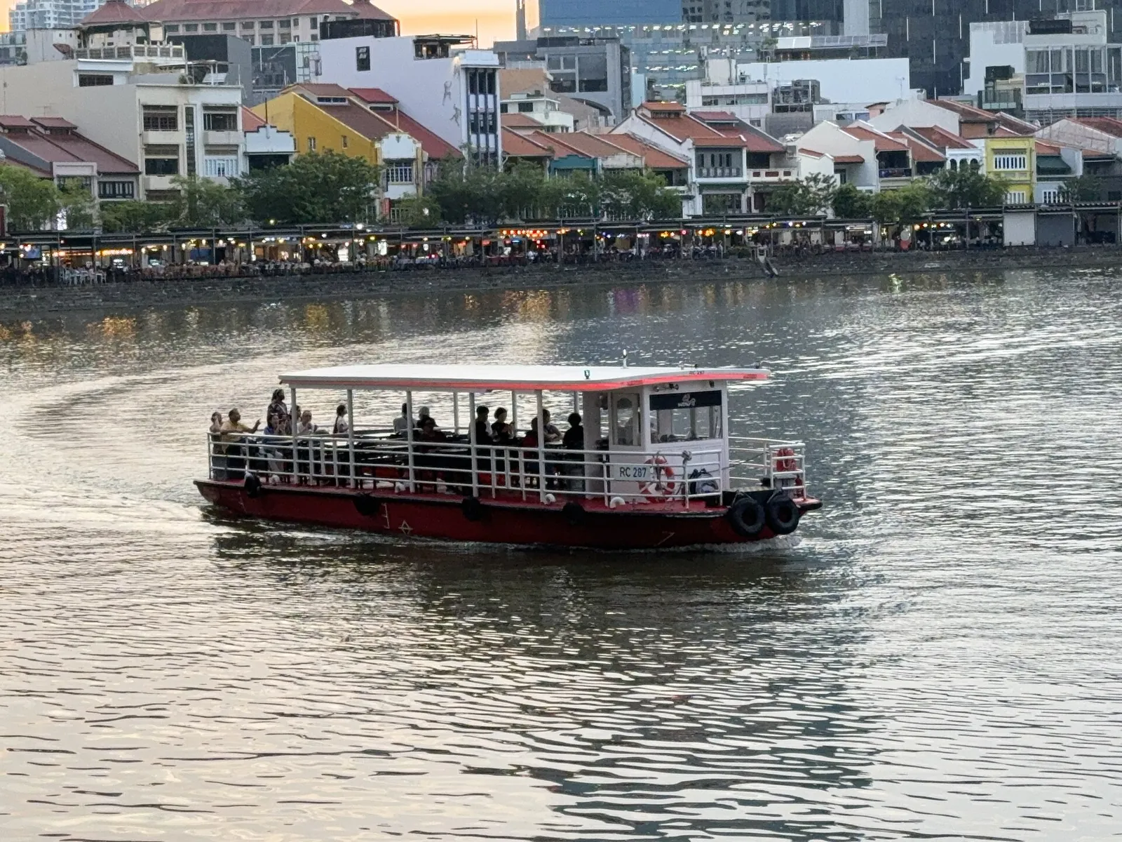 Osobní loď přejíždějící Singapore River s obchodními domy v pozadí