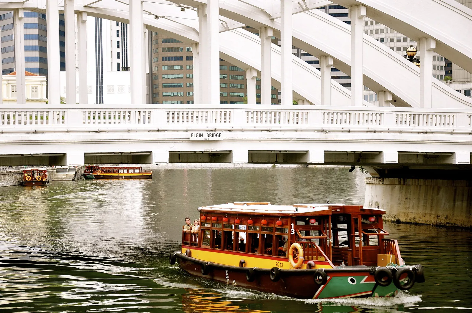 Een houten rivierboot vaart onder Elgin Bridge in Singapore door