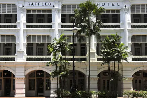 Facciata bianca del Raffles Hotel con palme e piano terra porticato