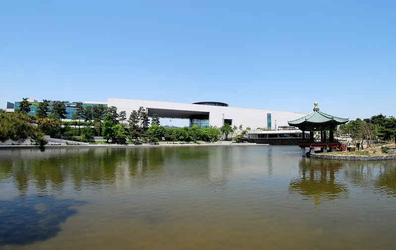 The National Museum of Korea in Seoul seen across its reflecting pond with a traditional pavilion, under a clear blue sky