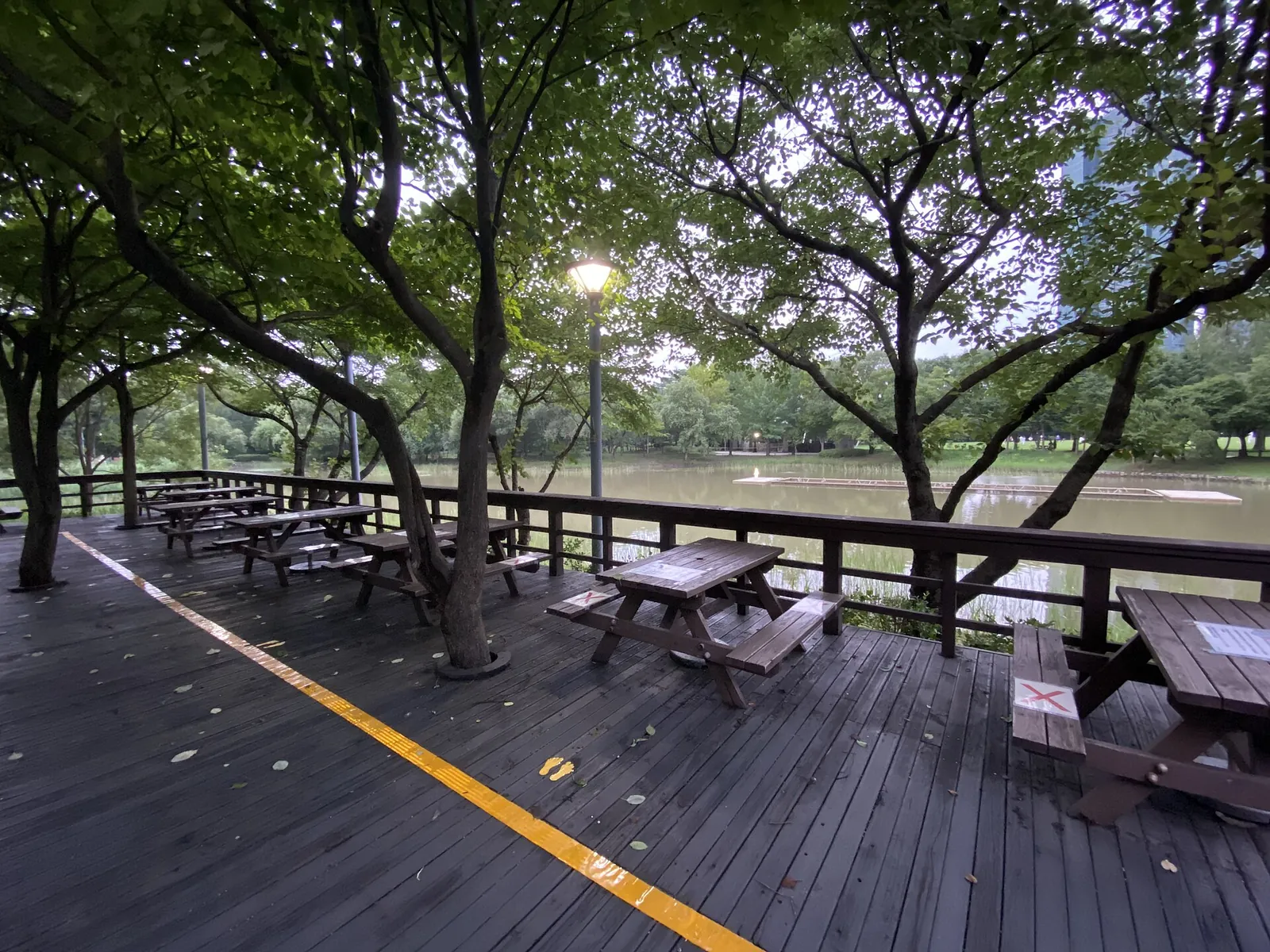 A wide wooden boardwalk with picnic tables under trees beside the water in Seoul Forest