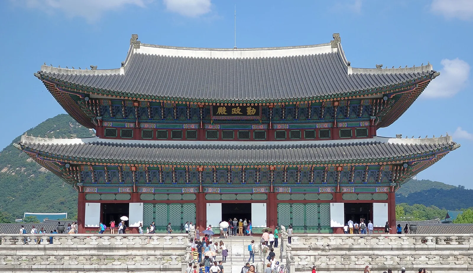Geunjeongjeon throne hall at Gyeongbokgung Palace in Seoul above its stone-paved courtyard, with visitors on the terraces