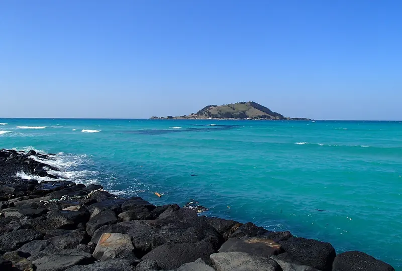 Turquoise sea breaking on black basalt rocks at Hyeopjae Beach, with the volcanic islet of Biyangdo on the horizon