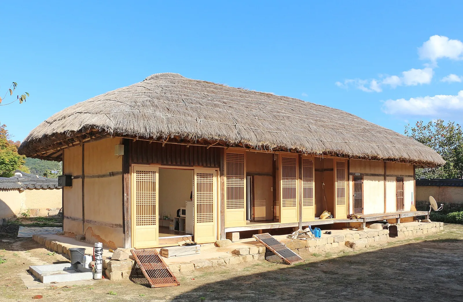 A thatched-roof hanok with a wooden veranda under a blue sky in Hahoe Village