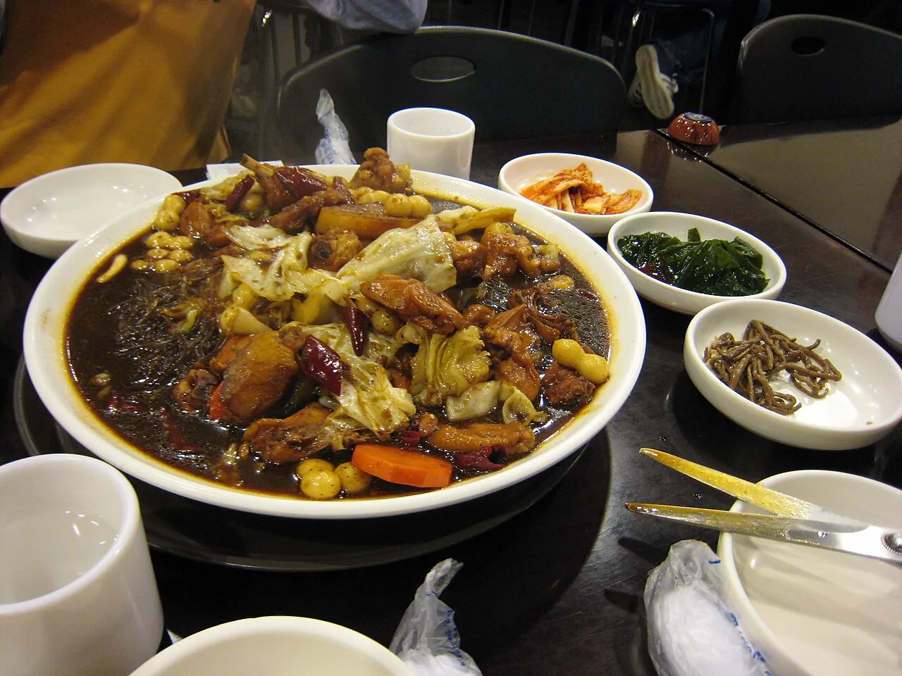 A large plate of Andong jjimdak with chicken, glass noodles and vegetables in dark soy sauce, with side dishes