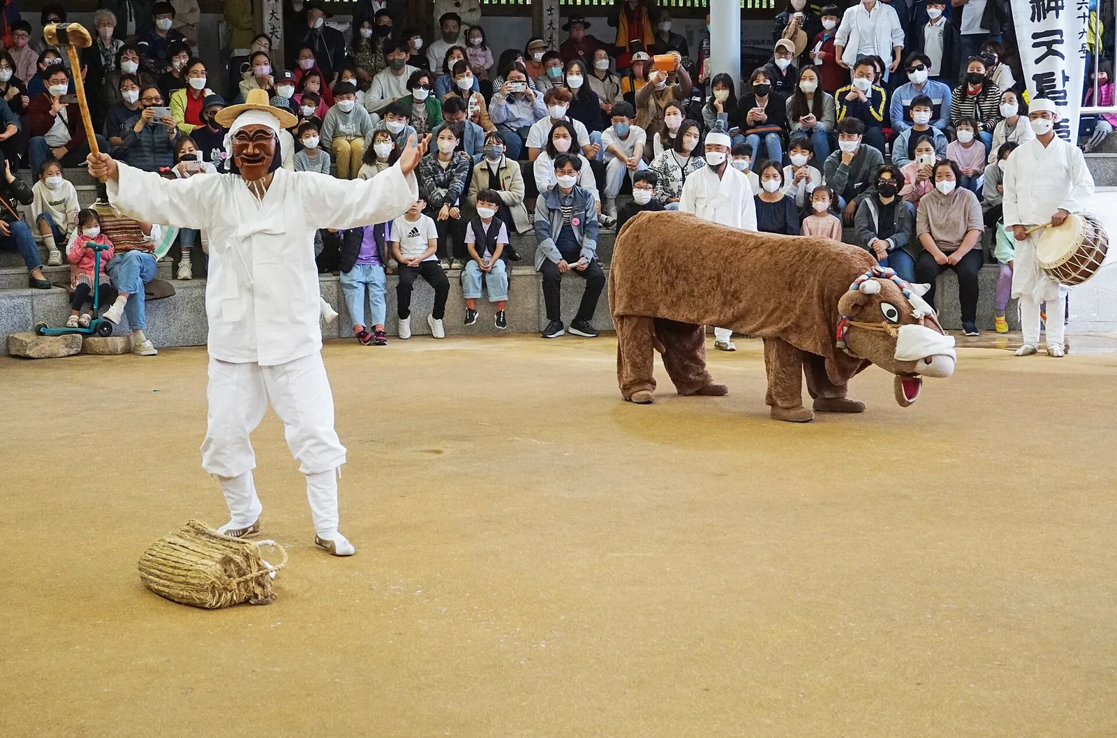 Hahoe mask dance performers in white costumes and a bull costume before a seated crowd