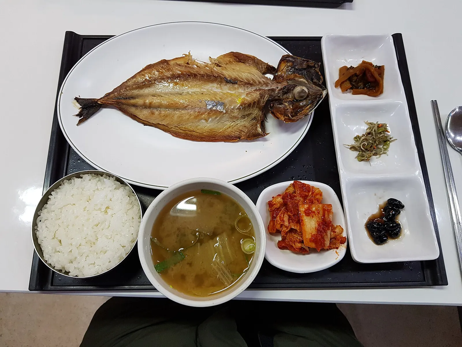 A grilled salted mackerel set meal with rice, soup, kimchi and side dishes on a tray