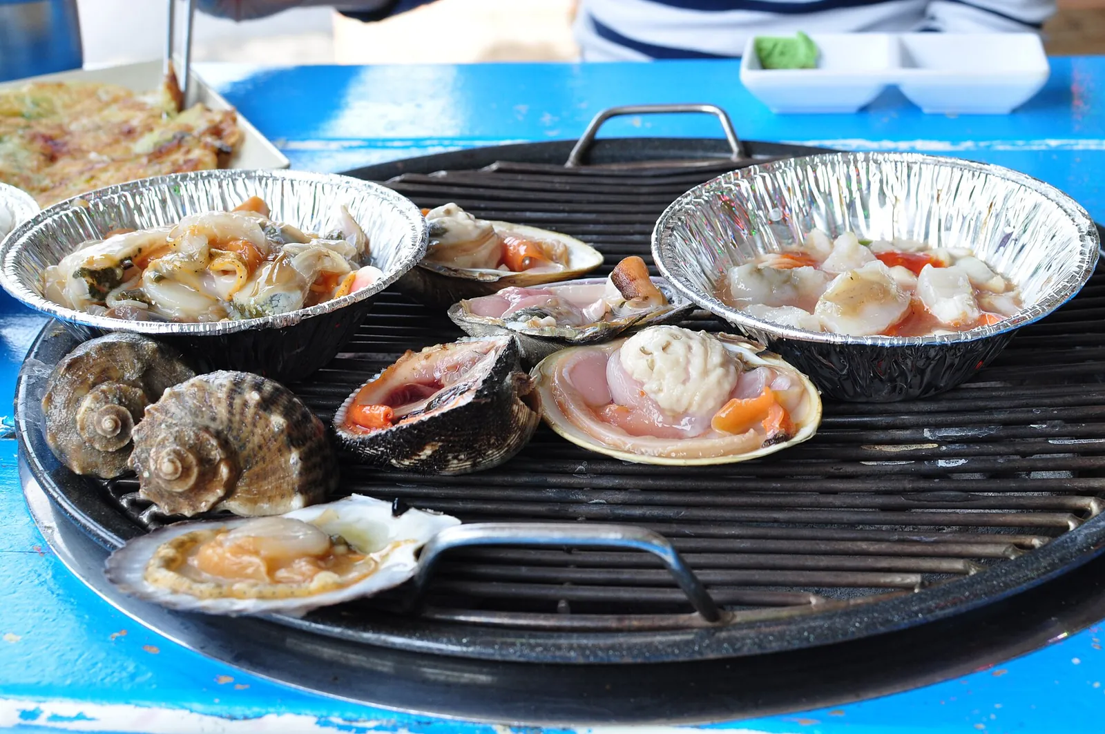 Scallops, clams and sea snails cooking on a round tabletop grill, a Korean grilled shellfish meal