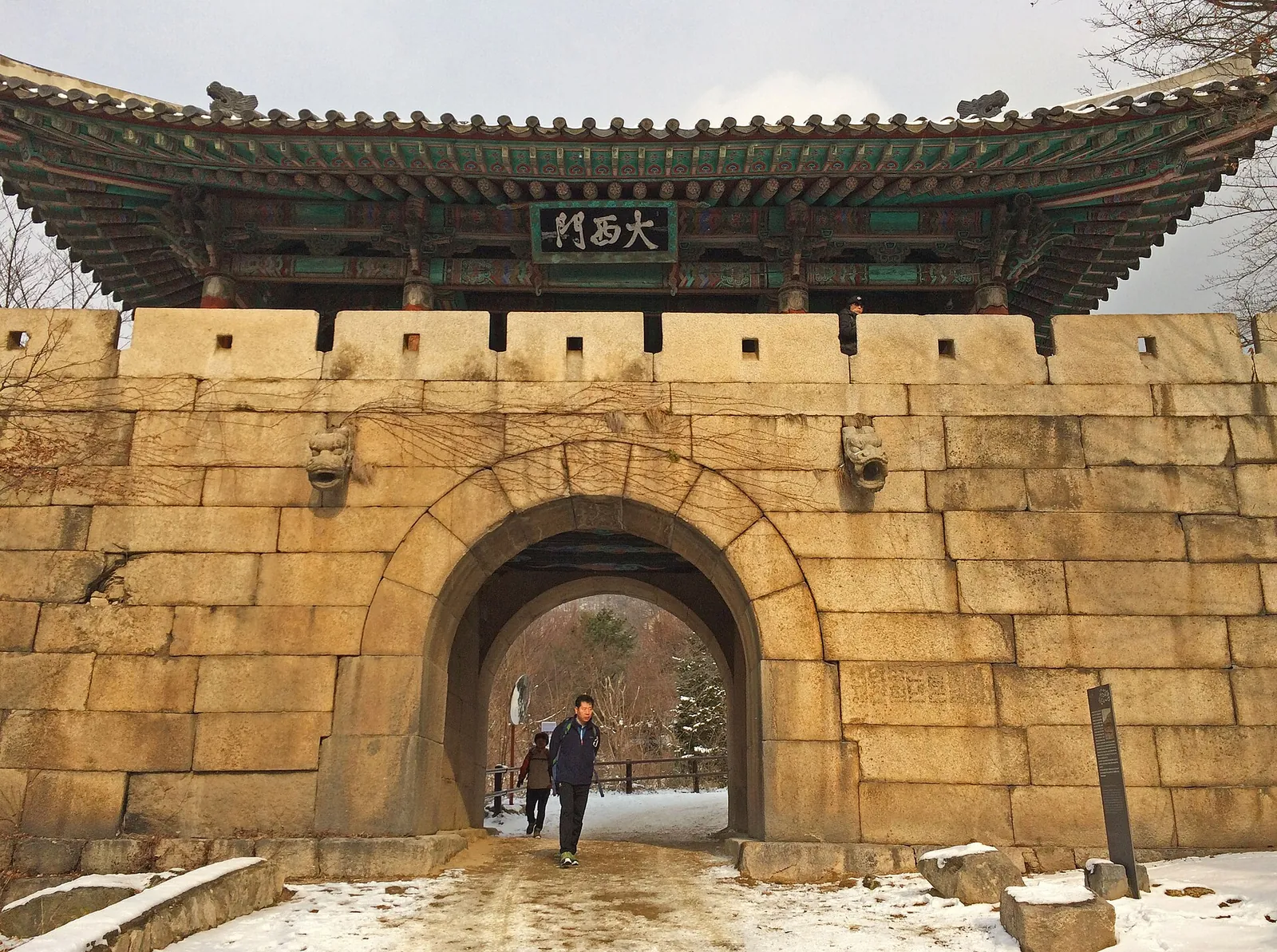 Stone arch gate of Bukhansanseong Fortress with a tiled pavilion roof and snow on the ground