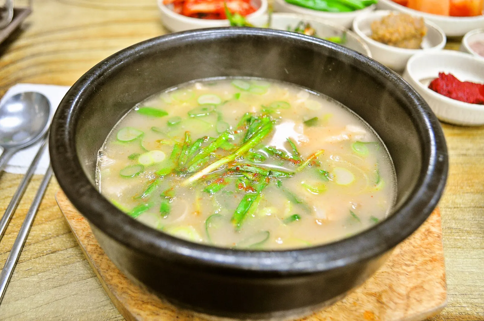 A stone bowl of dwaeji gukbap, pork and rice soup topped with spring onions, with side dishes