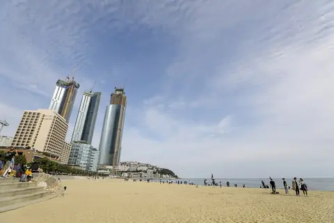 Haeundae Beach in Busan: a wide sand beach in daylight with the tall towers of the Haeundae district behind it