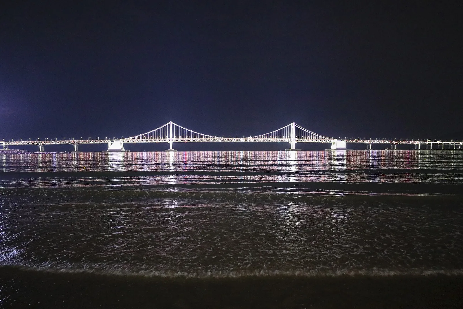 Gwangandaegyo Bridge lit up at night over the water, seen from Gwangalli Beach in Busan