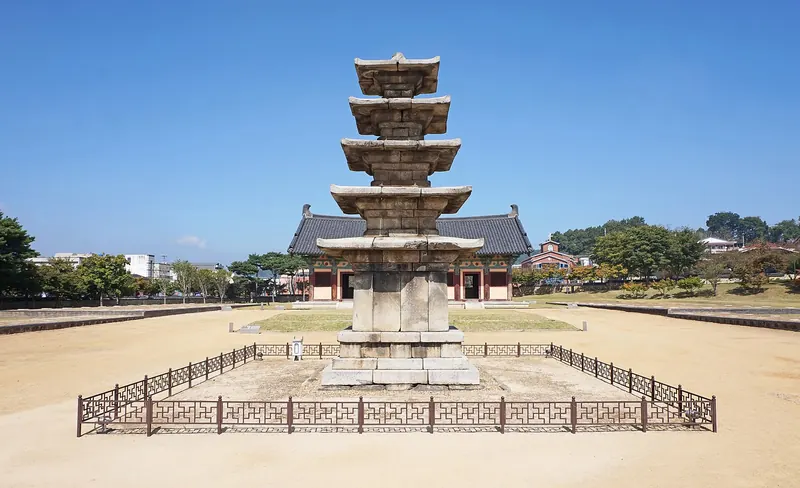 Five-storey stone pagoda at the Jeongnimsa Temple Site in Buyeo under a blue sky, with the museum hall behind