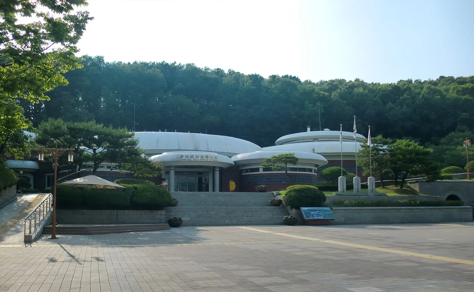 The low, domed buildings of the Cheongju Early Printing Museum seen across its forecourt, with wooded hills behind
