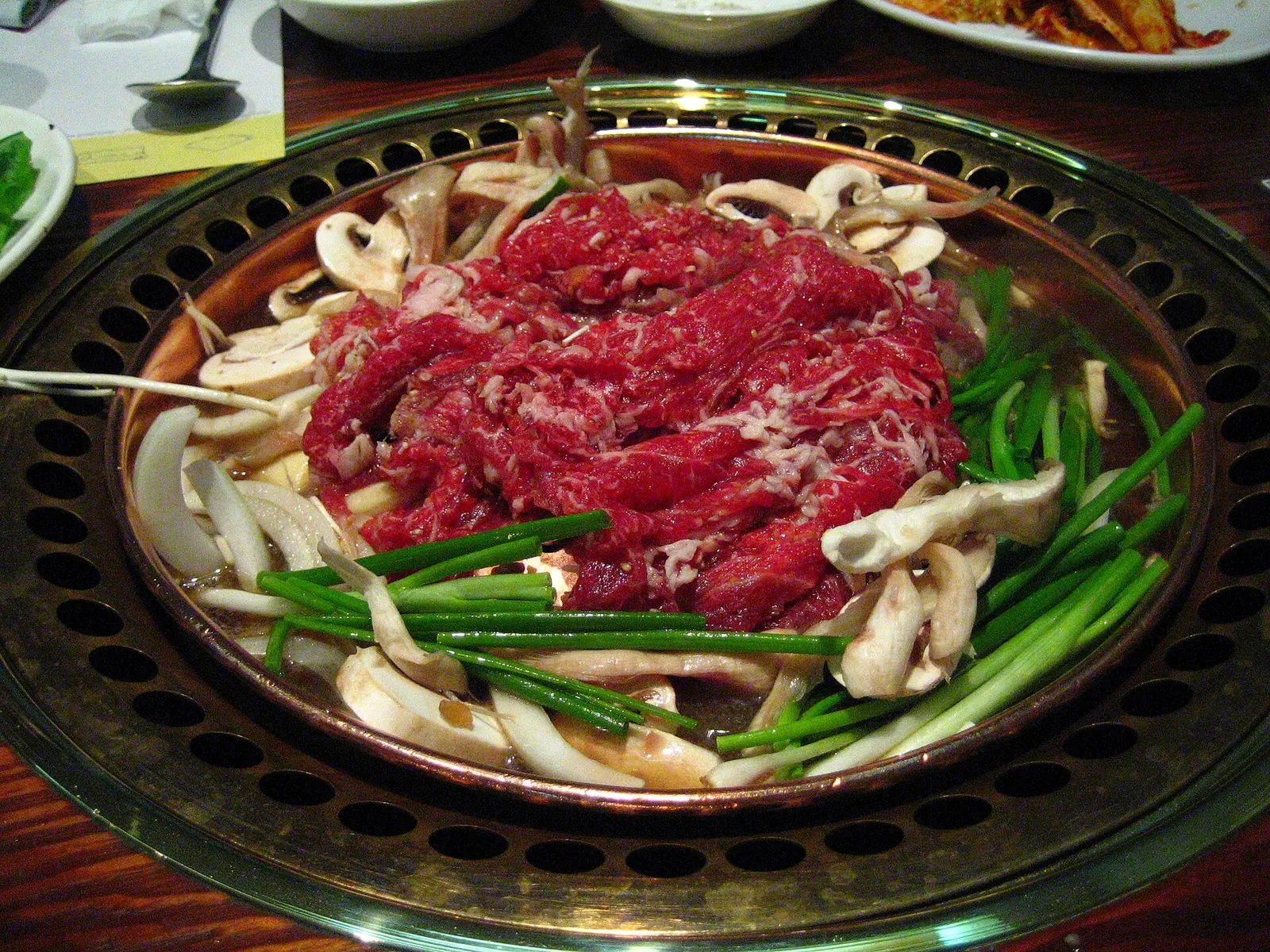Raw marinated beef bulgogi with mushrooms, onions and spring onions on a domed Korean grill pan