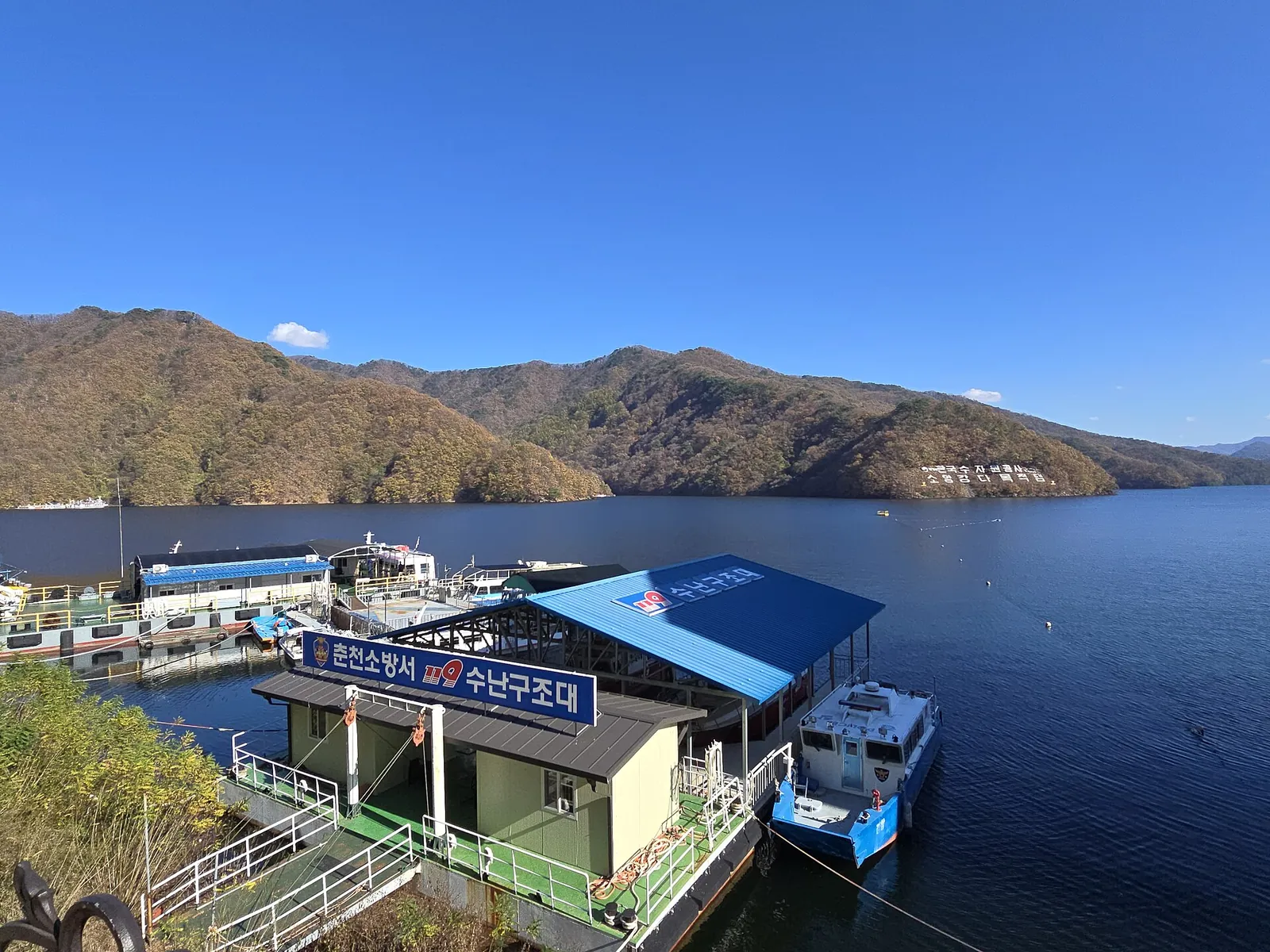Boats moored at a floating station on Soyangho Lake in Chuncheon, below autumn-coloured hills and a clear blue sky