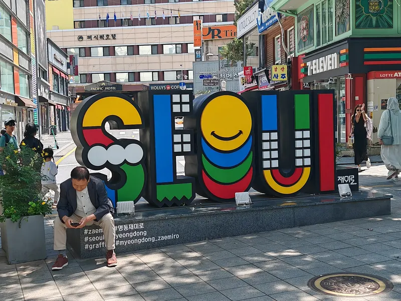 Colourful Seoul city sign on a pedestrian street in Myeongdong, Seoul, with shops and a 7-Eleven behind it