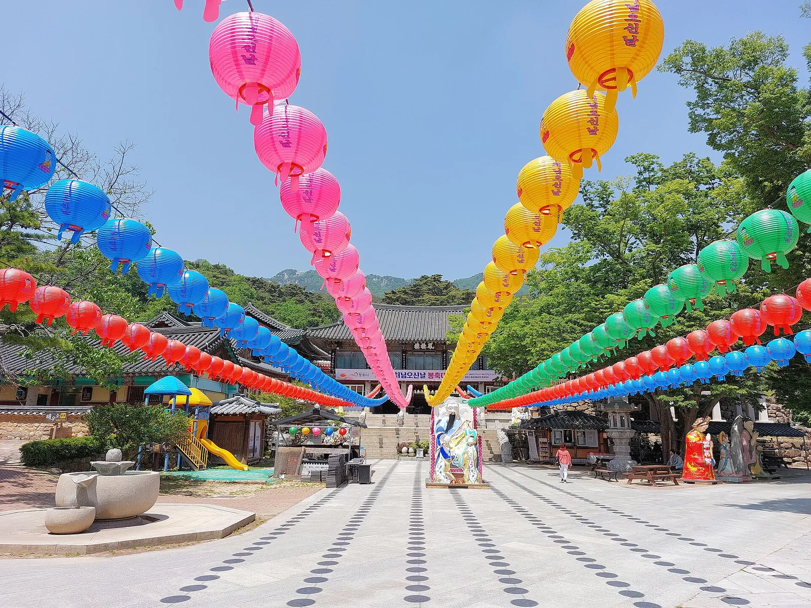 Rows of colourful paper lanterns strung across the stone courtyard of Donghwasa temple, with forested hills behind