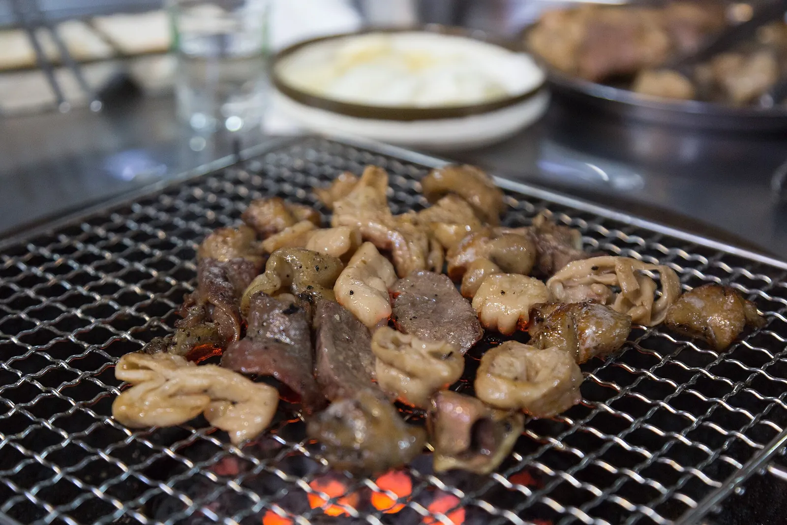 Pieces of makchang (pork intestines) grilling on a table grill over charcoal