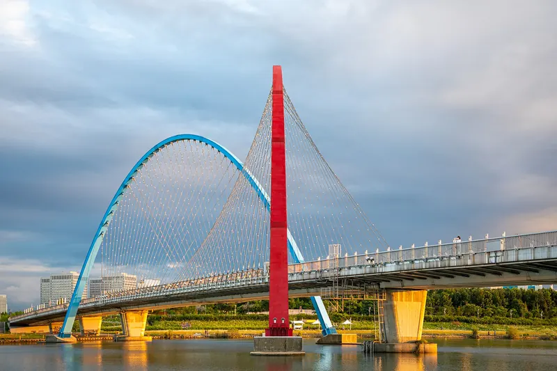 The red-and-blue arches of the Expo Bridge over the Gapcheon in Daejeon under a partly cloudy sky