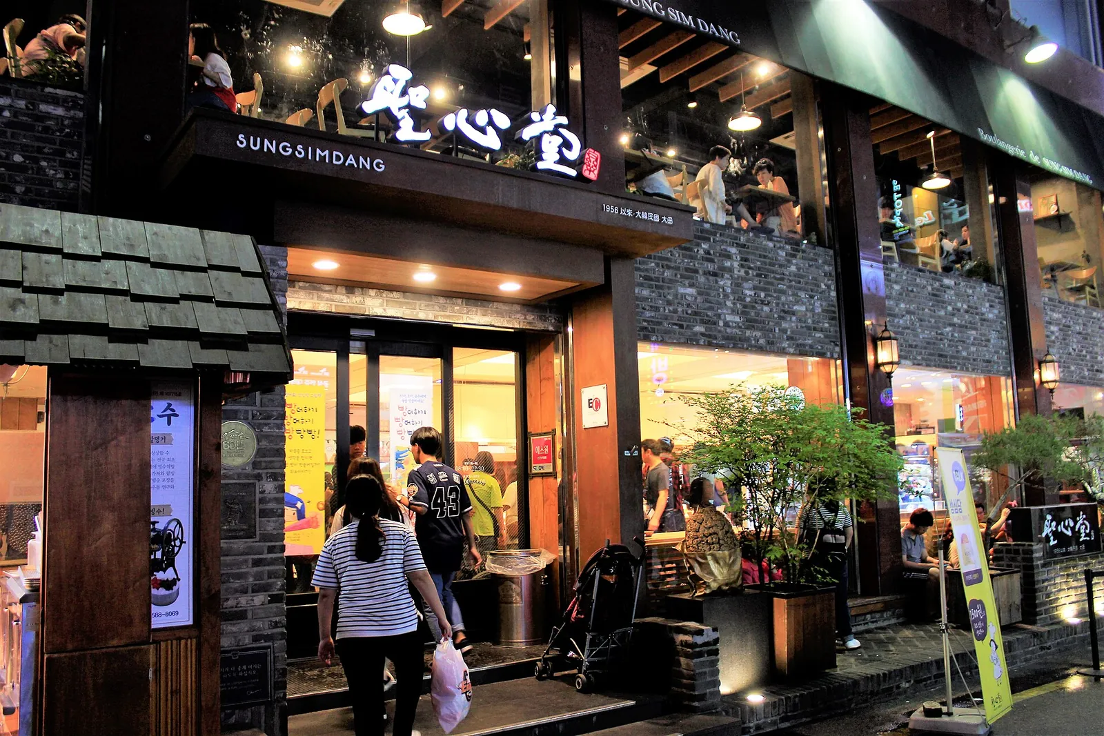 Shoppers outside the entrance of a Sungsimdang bakery store in Daejeon, with its signboard lit