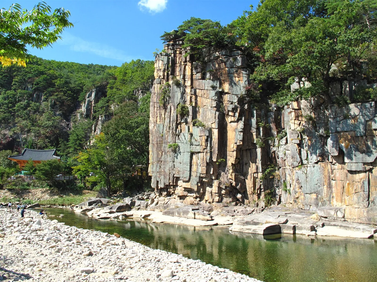 The sheer, column-like granite face of Sainam Rock above a clear stream in summer