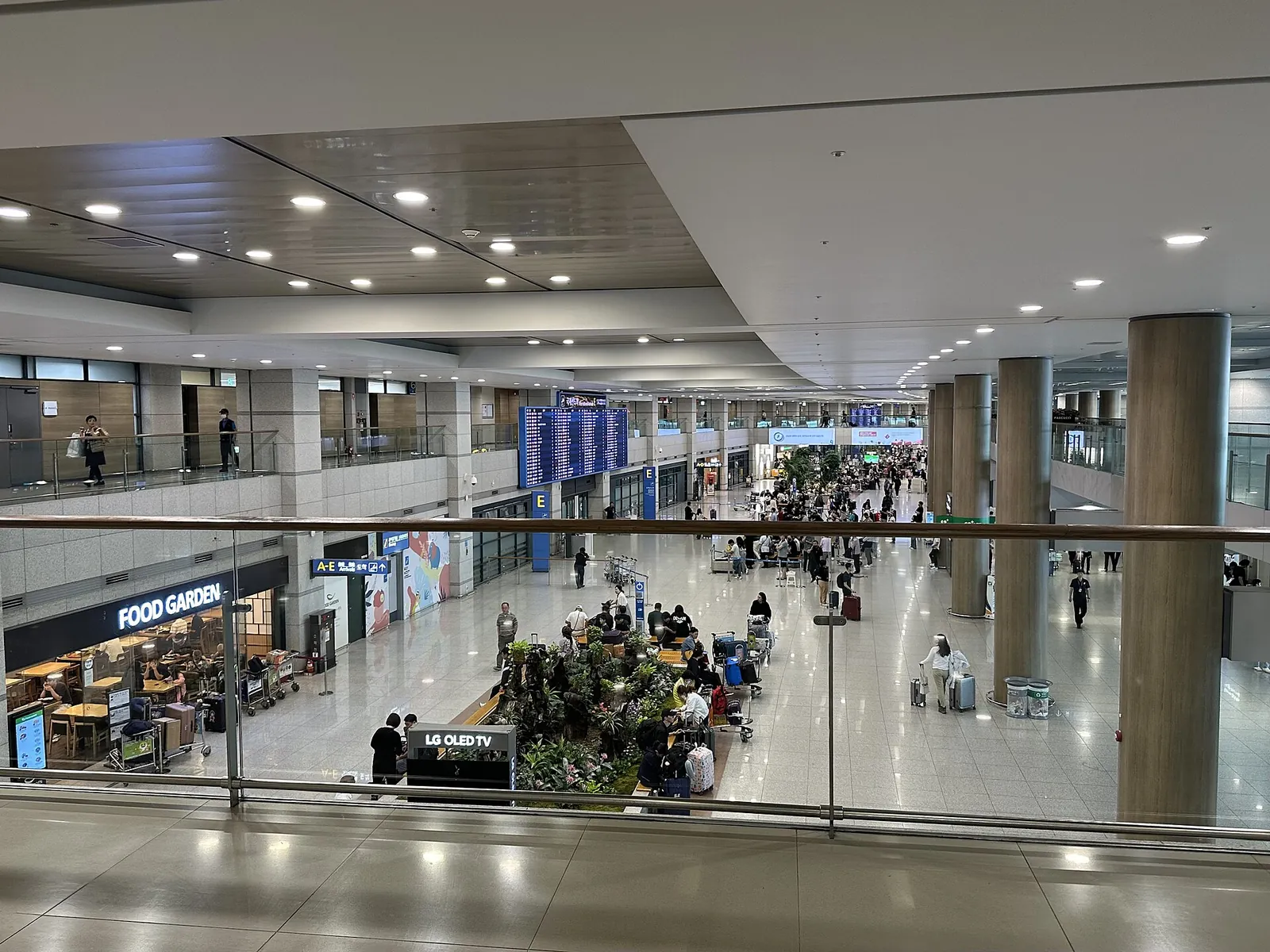Bright arrivals hall of Incheon International Airport Terminal 1 seen from the upper floor, with a food court and travellers below
