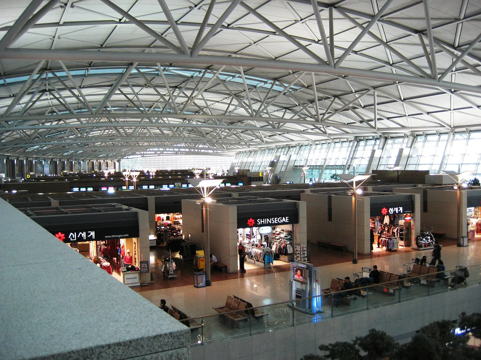 Departure hall of Incheon International Airport under a curved steel-truss roof, with duty-free shops below