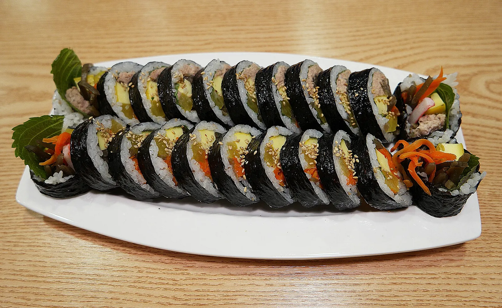 A long plate of sliced gimbap, Korean rice and seaweed rolls filled with vegetables, egg and meat