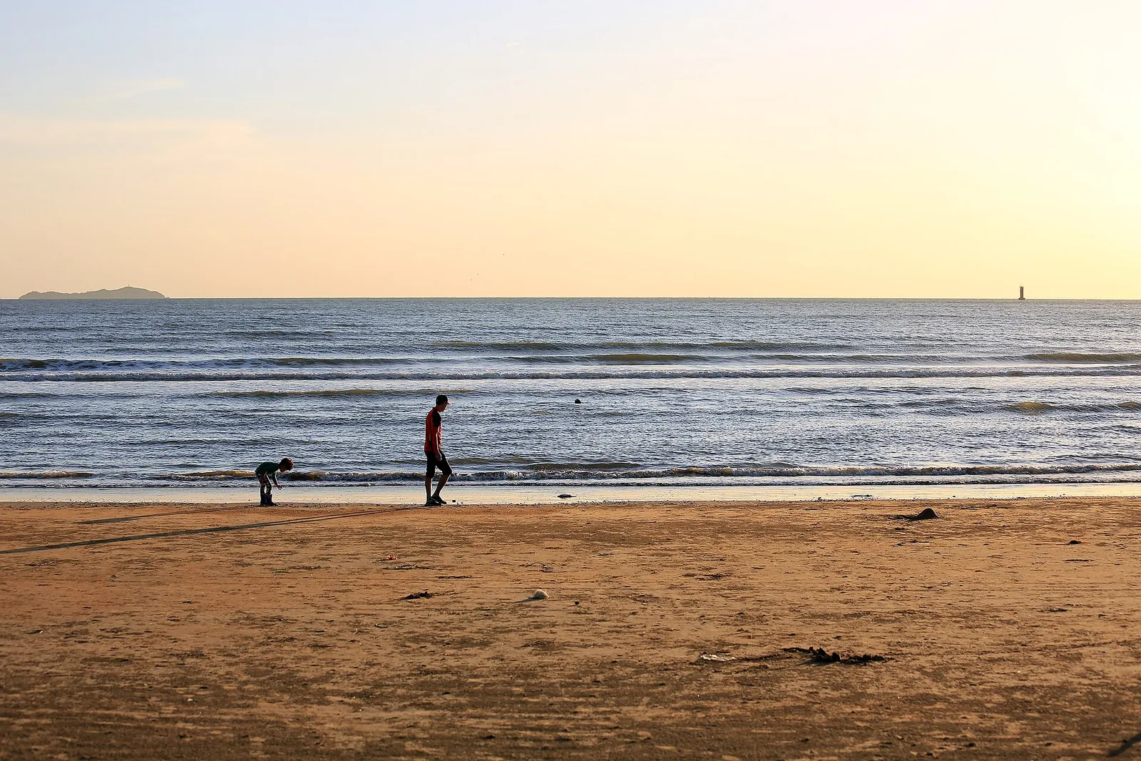 Two people on the wide sandy beach at Mongsanpo in Taean in low golden light, one bending down at the water's edge