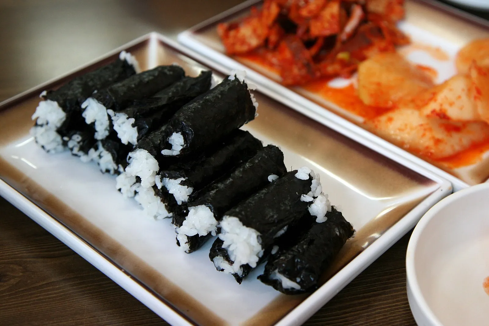 Finger-sized Chungmu gimbap rolls of plain rice in seaweed, with spicy radish kimchi and squid salad on the side